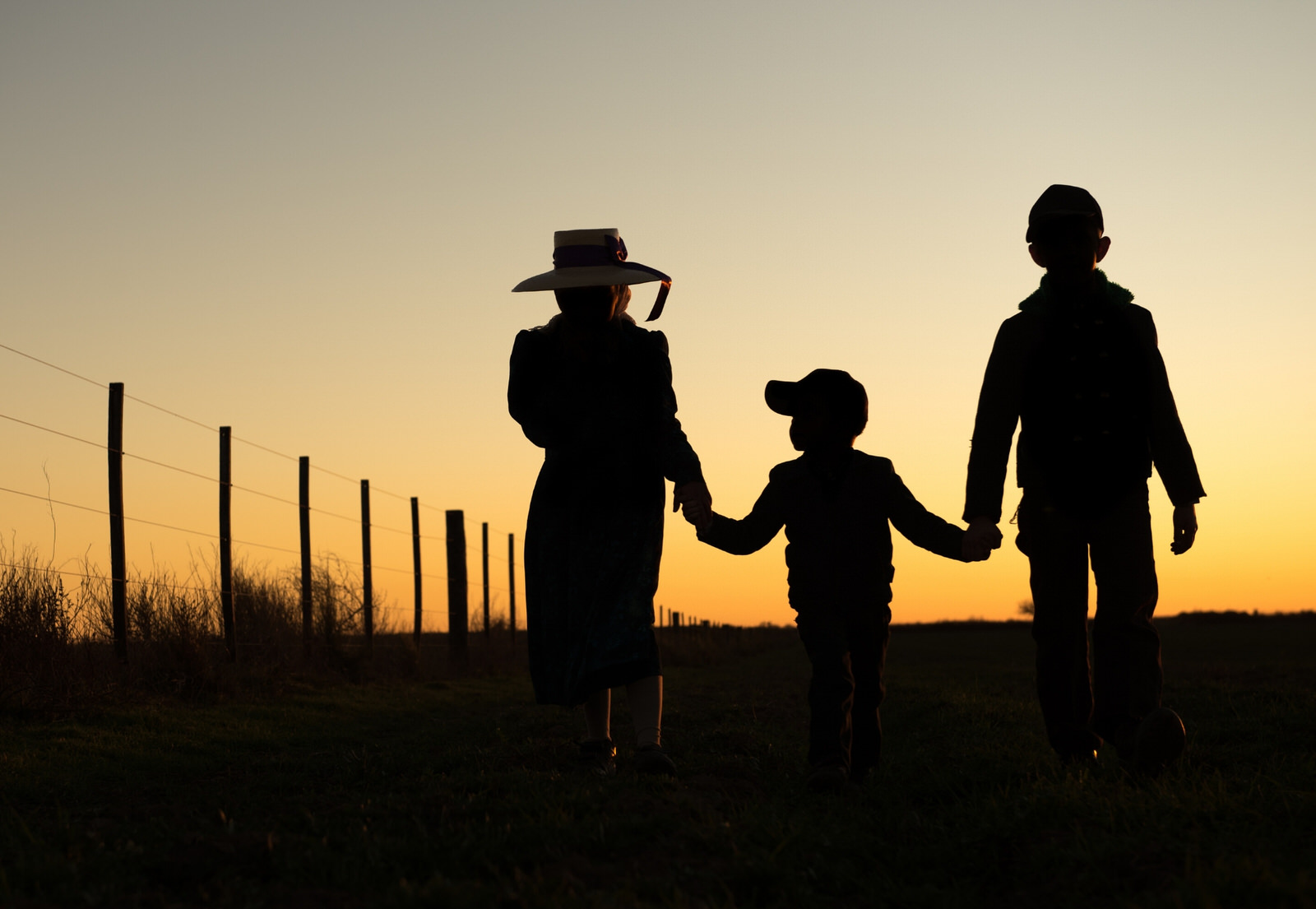Three people taking a walk in a ranch at sunset.